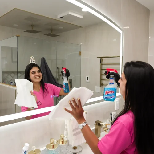 Professional cleaner spraying and wiping residential bathroom vanity mirror
