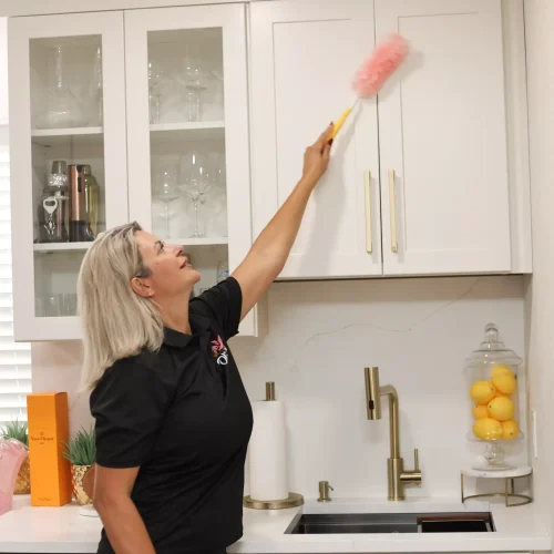 Maid cleaning kitchen backsplash wall and upper cabinet surfaces