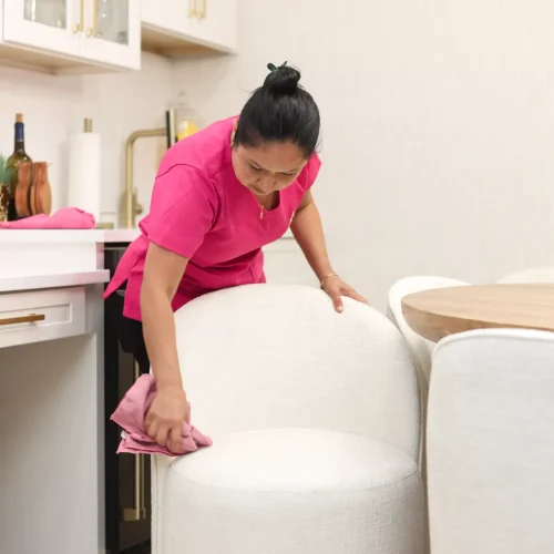 Maid cleaning the sides and frame of a plush white dining chair