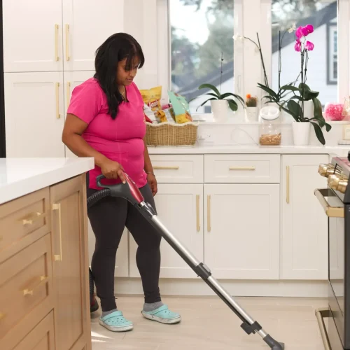 Professional maid using a stick vacuum cleaner on residential kitchen floor